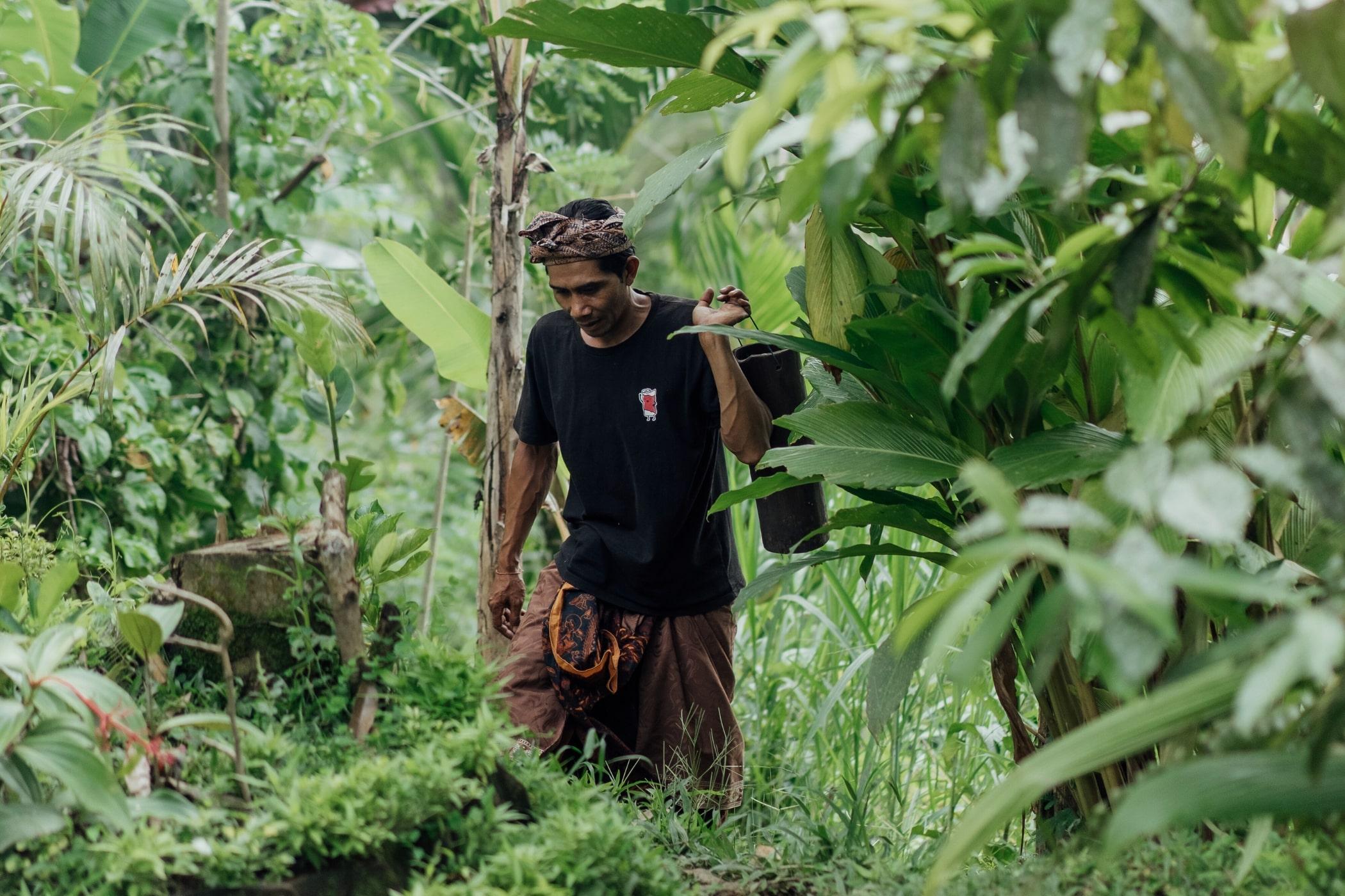 Man carrying tool walks through lush greenery at Banyan Tree Escape - Buahan - Stay for Good.