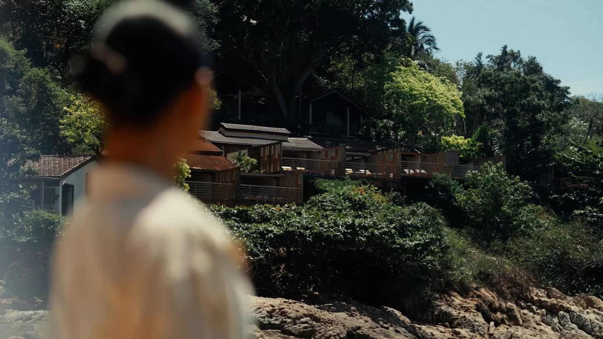 A person gazes at hillside wooden villas surrounded by lush greenery at A Banyan Tree Escape.