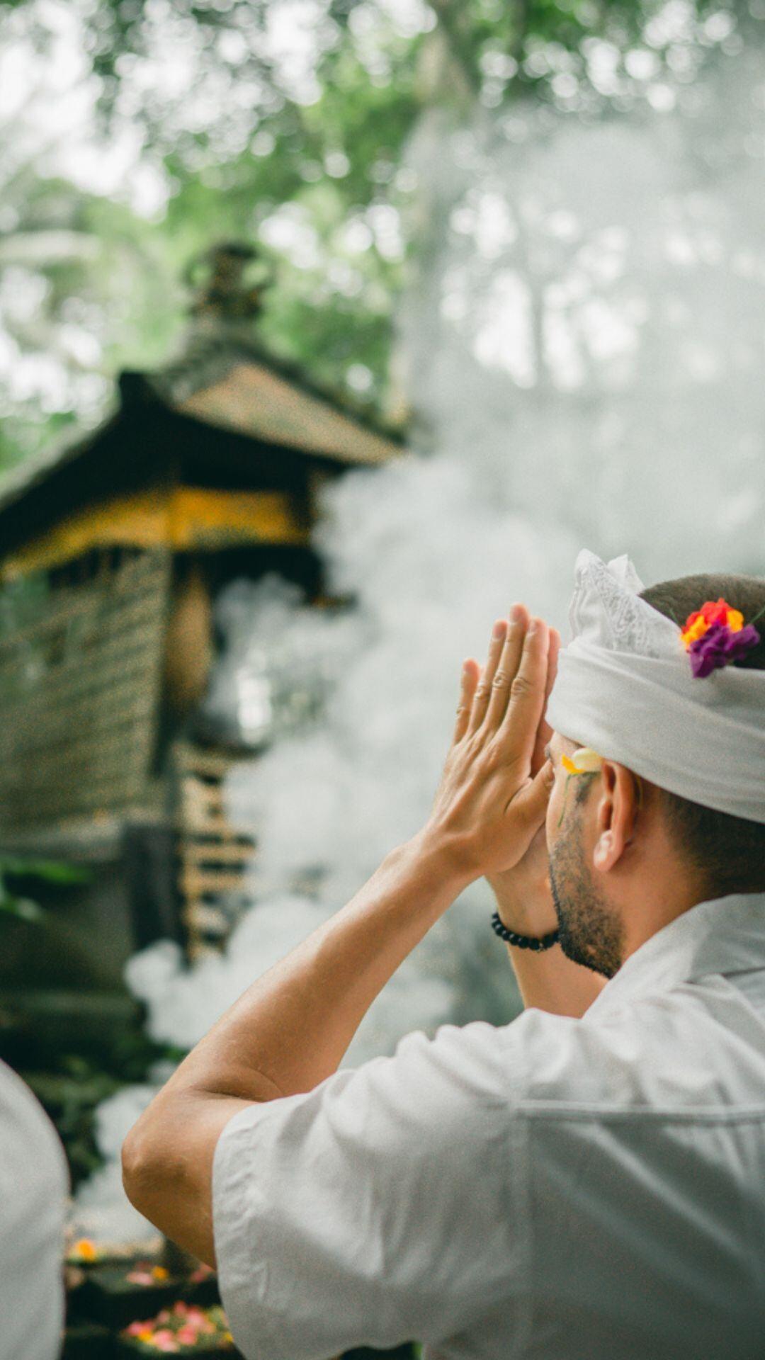 A person prays at a shrine amidst smoke and trees, Banyan Tree Escape - Buahan ambiance.