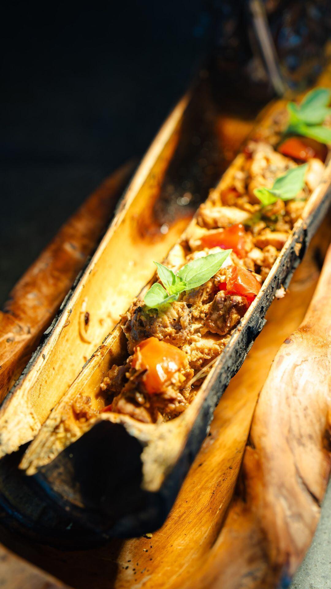 Rustic wooden tray with a savory dish at Banyan Tree Escape - Buahan, garnished with fresh herbs.