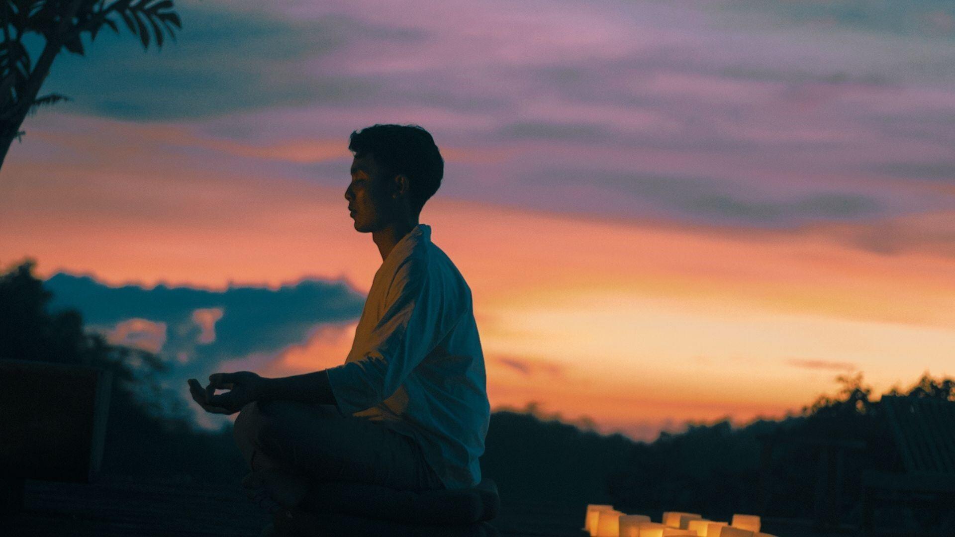 Person meditating at sunset, surrounded by candles at Banyan Tree Escape - Buahan resort.