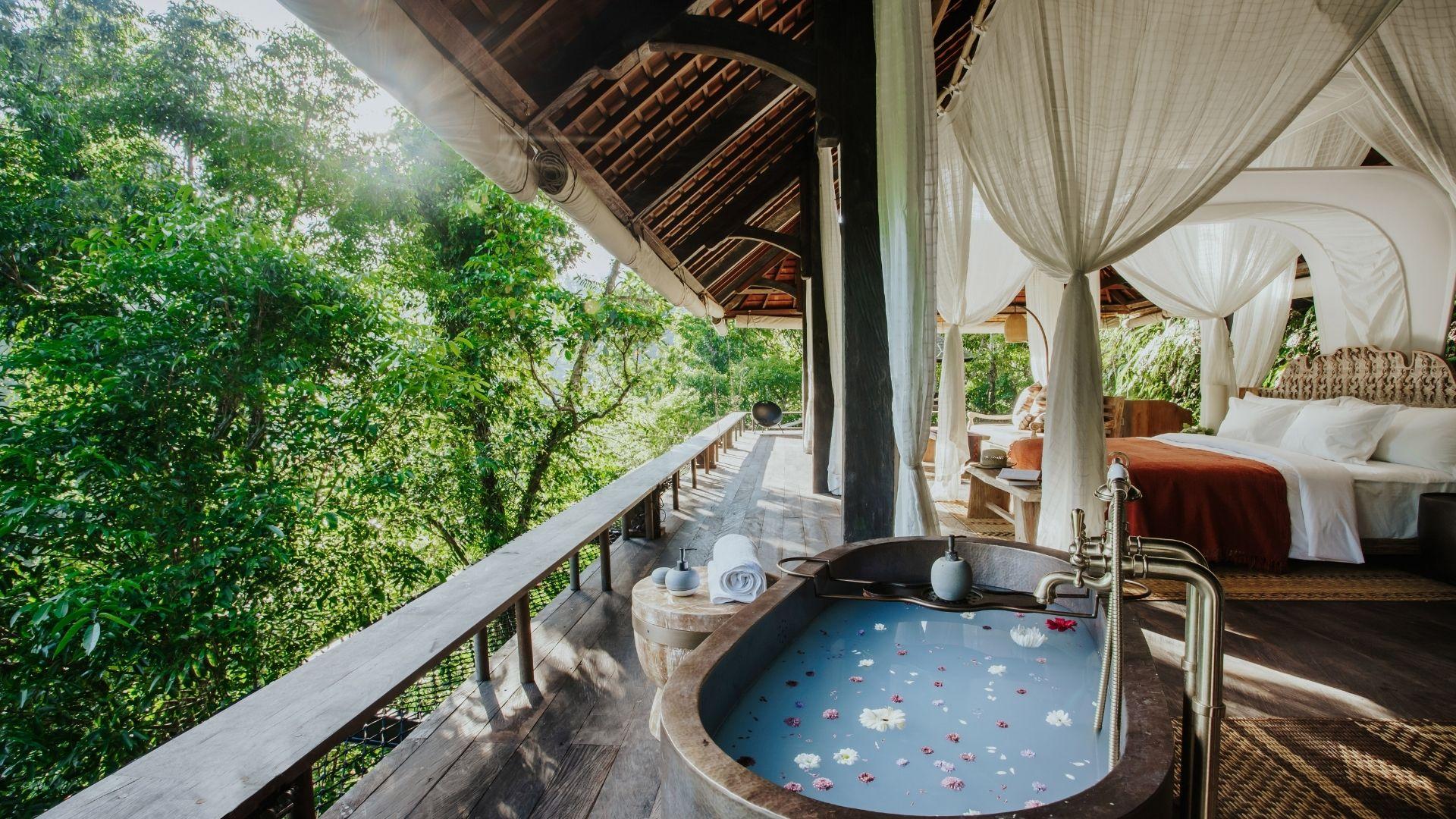 Outdoor tub with petals sits on a Banyan Tree Escape - Buahan villa above the waterfall balcony, surrounded by lush greenery.