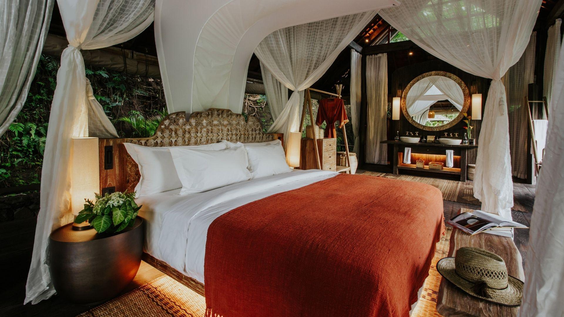 Luxurious bed with canopy at Banyan Tree Escape - Buahan, surrounded by nature, wooden decor, mirror.