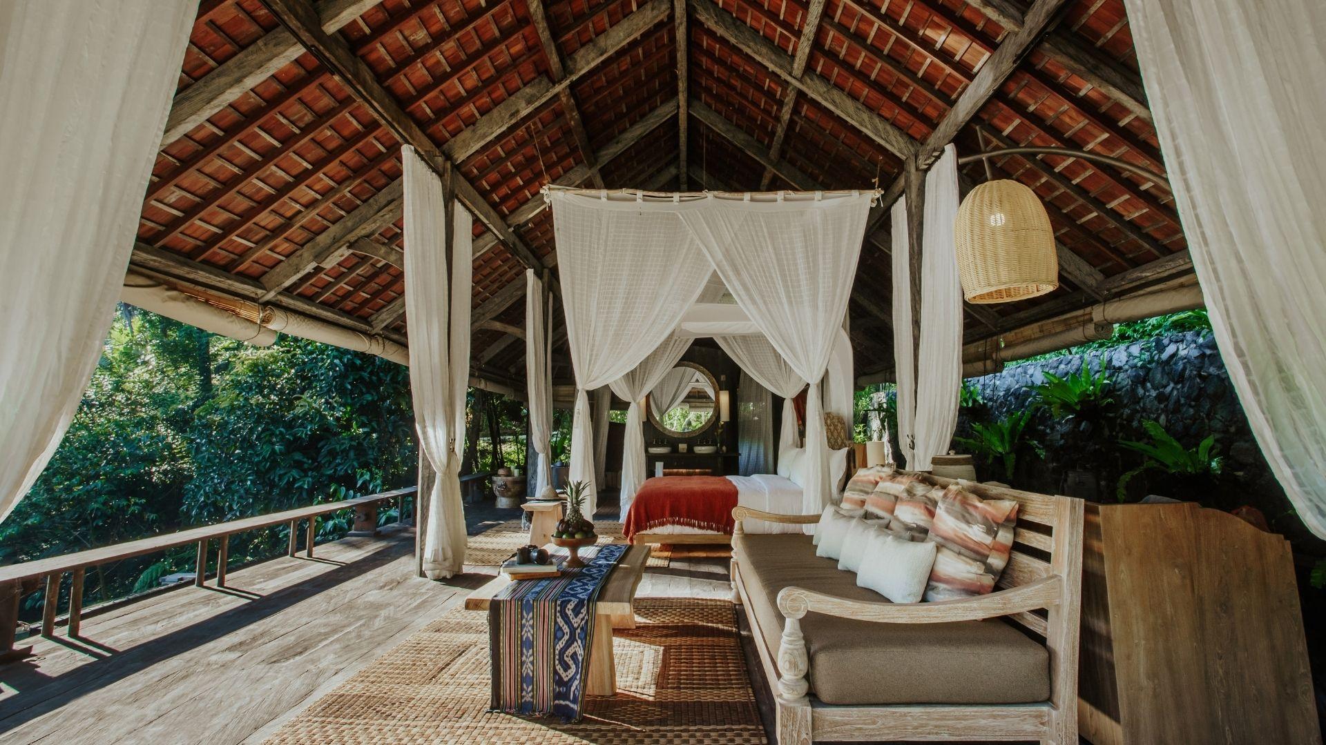 Open-air suite with rustic decor and canopy bed, surrounded by lush greenery at Banyan Tree Escape - Buahan.