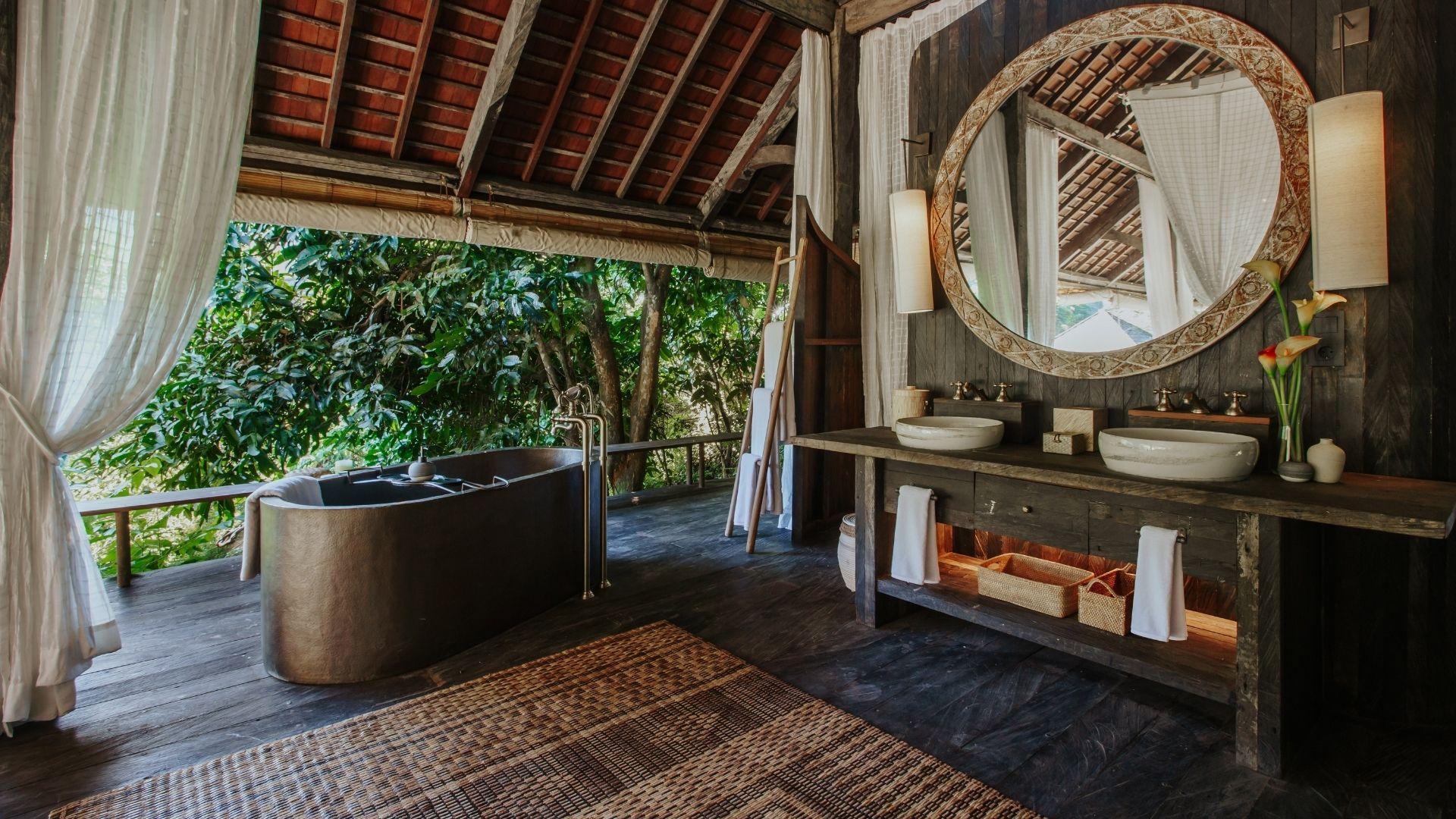 Luxurious bathtub overlooks lush rainforest in Banyan Tree Escape - Buahan, with dual sinks and large mirror.