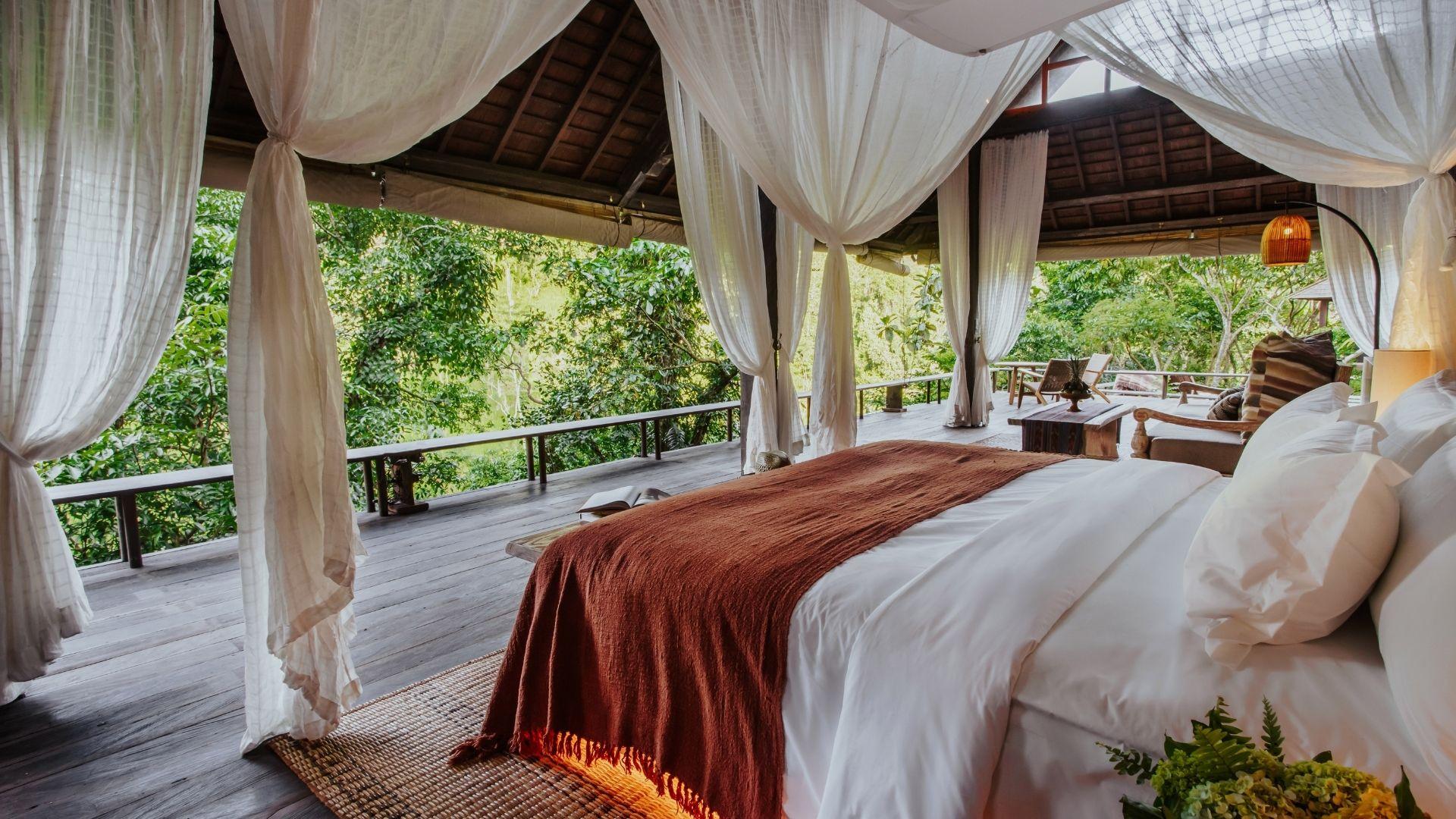 Canopy bed in open-air suite, draped with white curtains, overlooking lush forest at Banyan Tree Escape - Buahan.