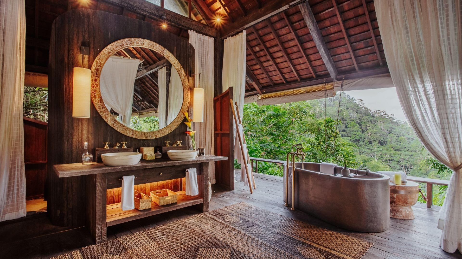 Luxurious open-air bathroom with round mirror, double sinks, and bathtub overlooking lush greenery at Banyan Tree Escape - Buahan.