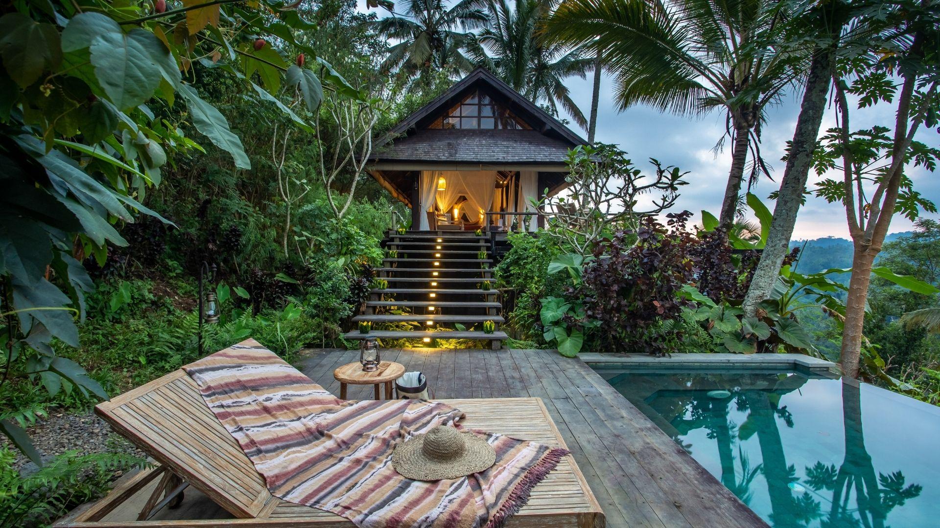 Lounge chair with hat faces lit pathway to villa, surrounded by lush greenery, at Banyan Tree Escape - Buahan.