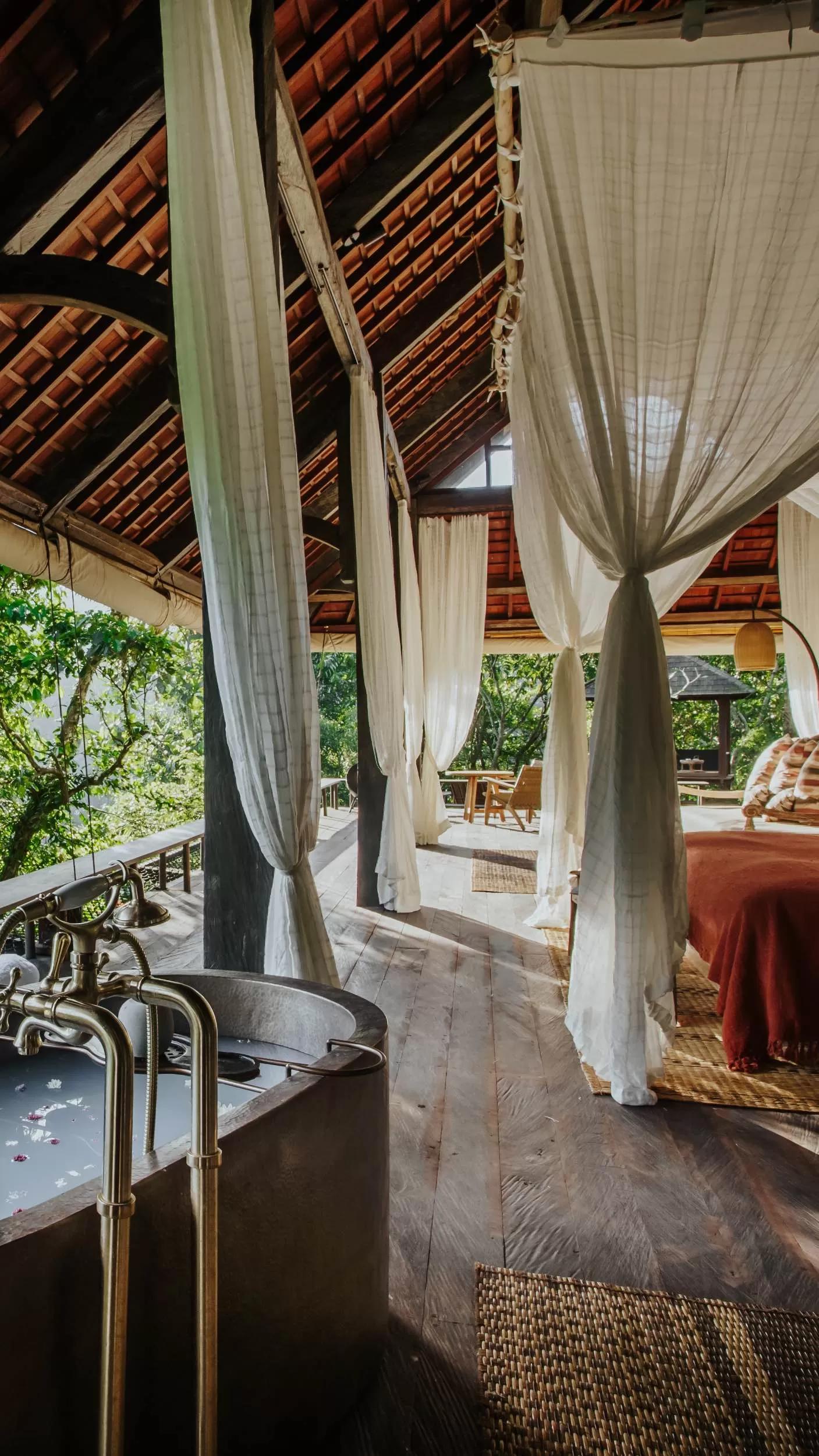 Bathtub filled with petals sits in open, airy villa lit by natural light at Banyan Tree Escape - Buahan.