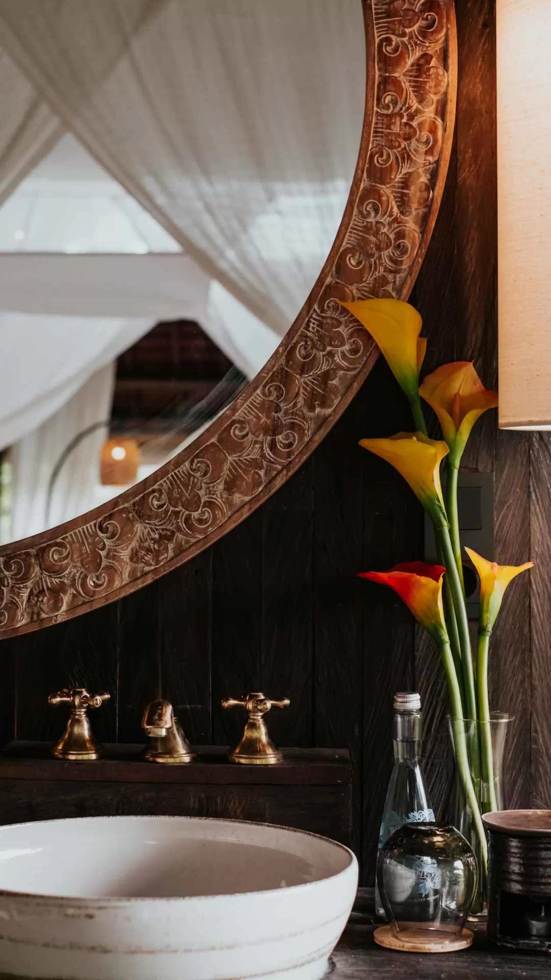 Decorative mirror reflects, vases hold vibrant flowers; serene Banyan Tree Escape - Buahan ambiance.