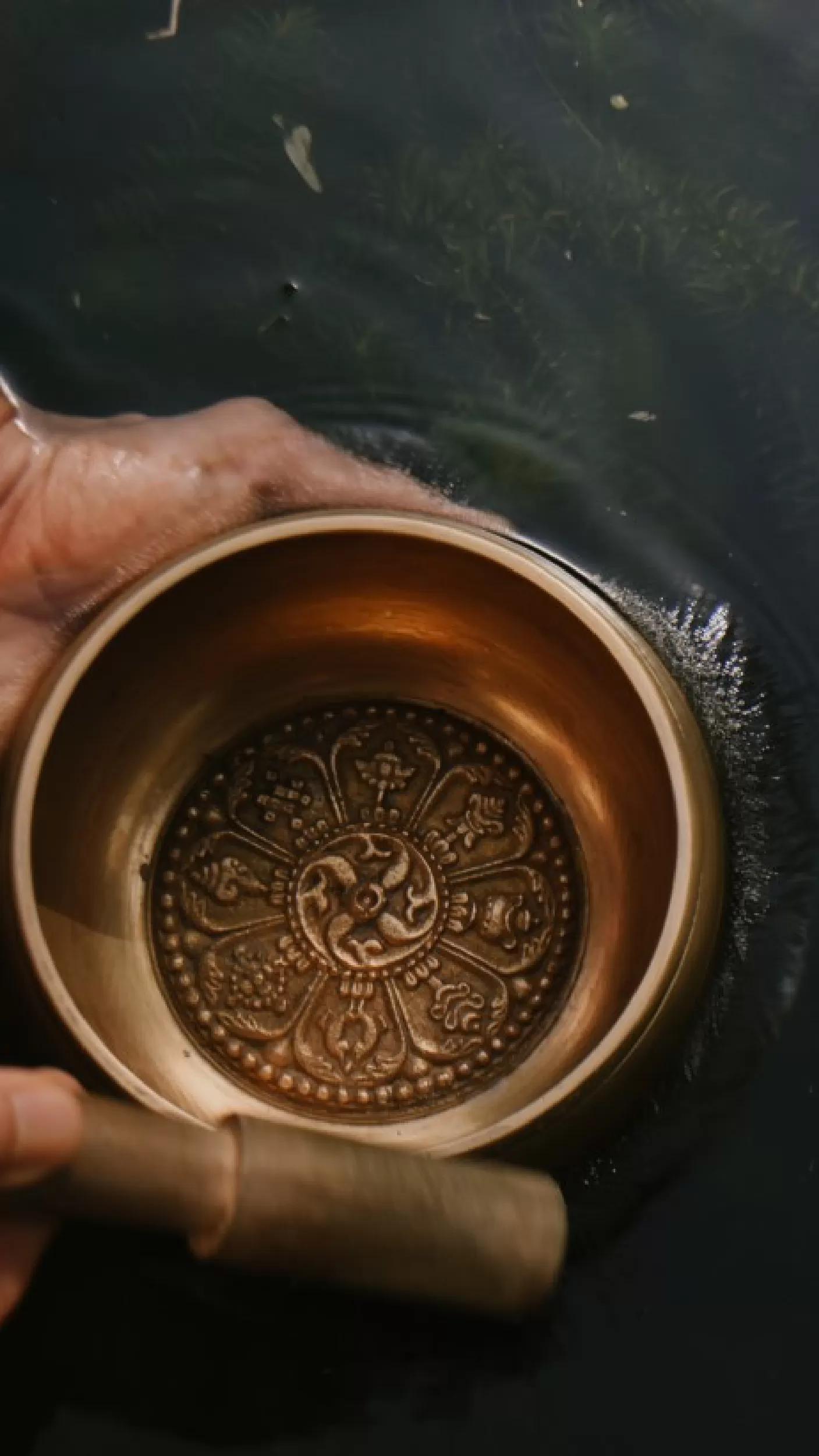 Hand holds ornate bowl, gently immersed in water at Banyan Tree Escape - Buahan Toja Spa.