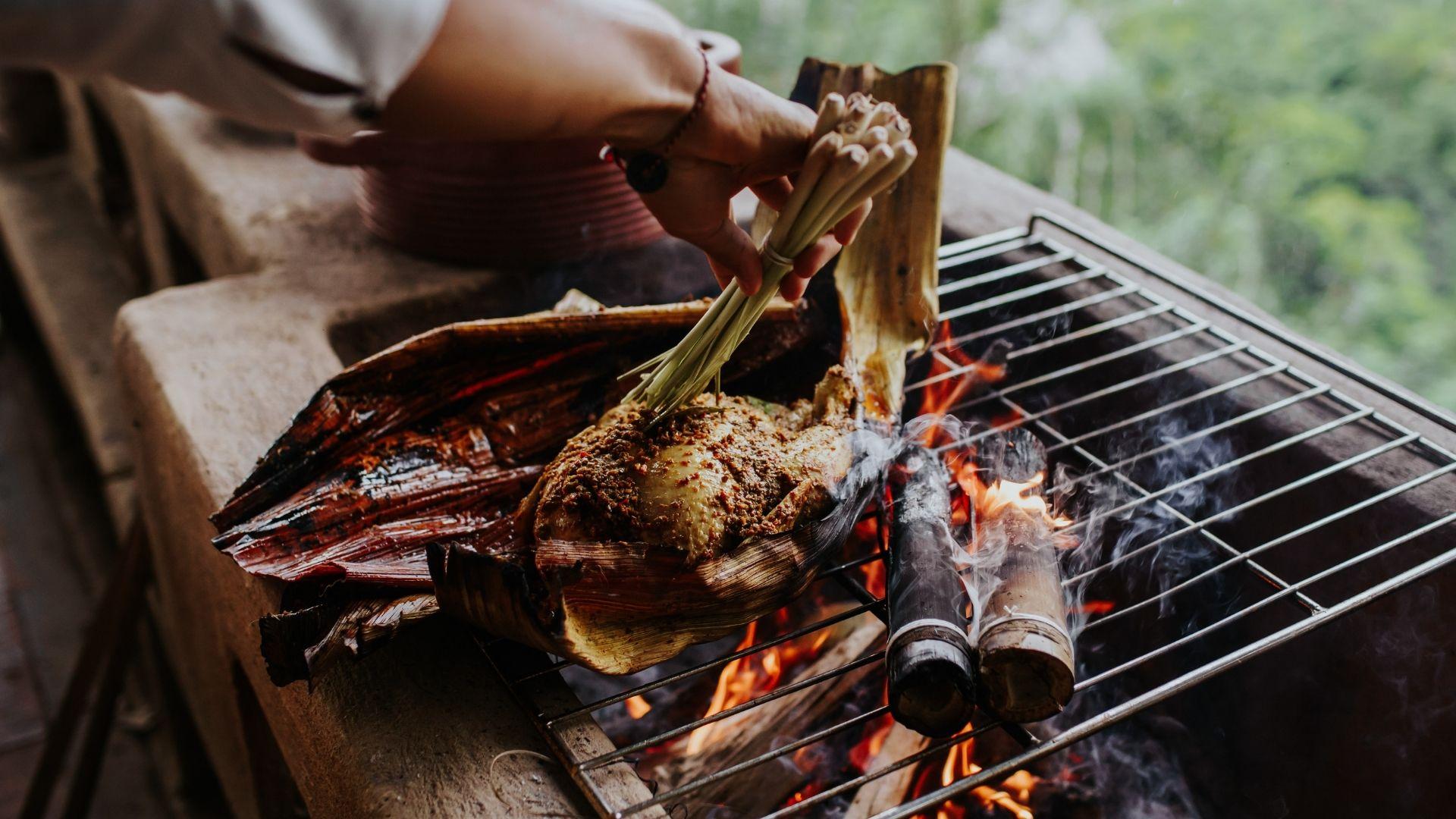 Hand grill-cooking spiced chicken wrapped in leaves at Banyan Tree Escape - Buahan.