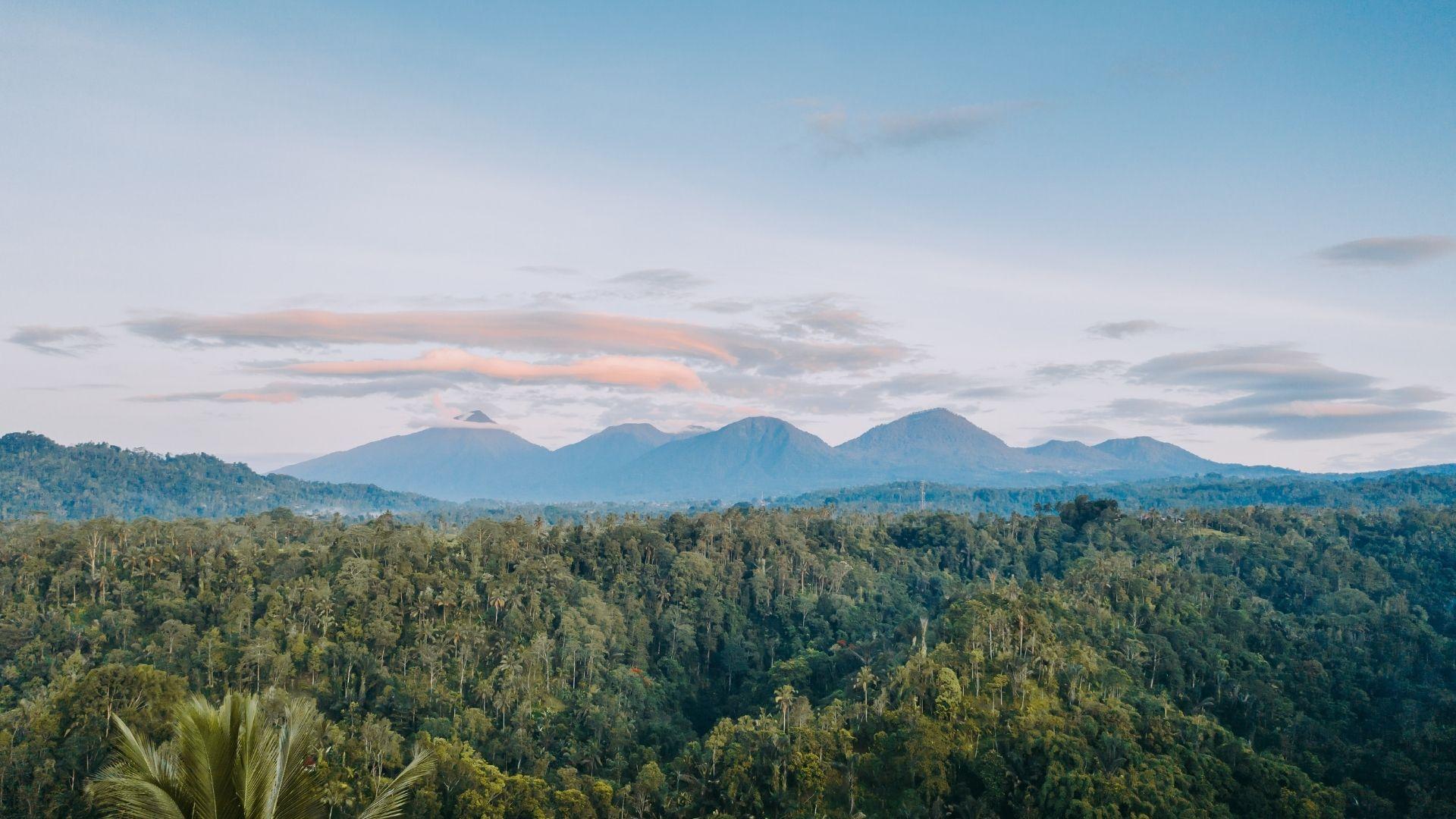 Mountains rise above lush forest under a serene sky, capturing Banyan Tree Escape - Buahan's tranquility.