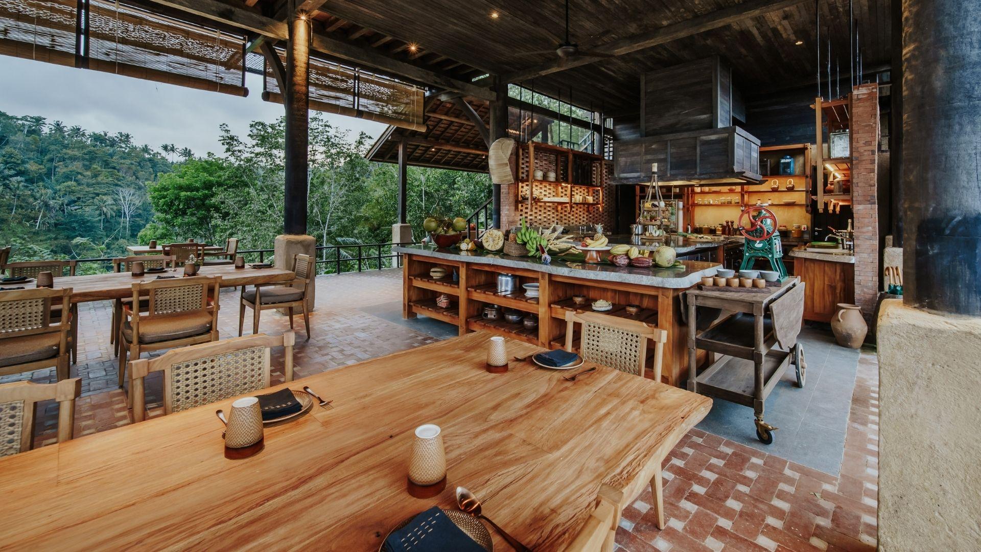 Open kitchen restaurant with wooden tables overlooking lush forest at Banyan Tree Escape - Buahan.