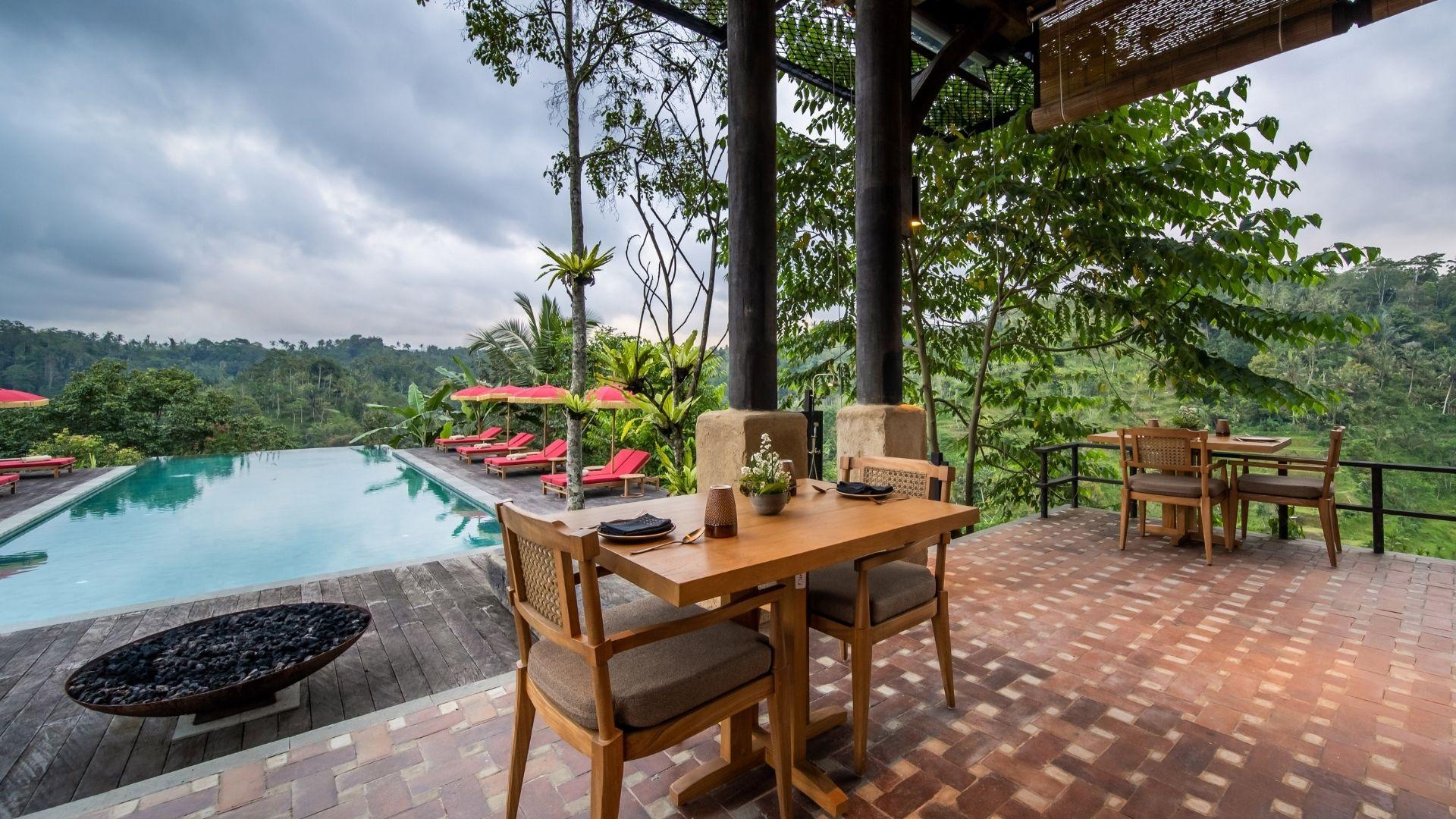 Poolside dining area of Open Kitchen Restaurant, overlooking lush valley; Banyan Tree Escape - Buahan. Cloudy skies above.