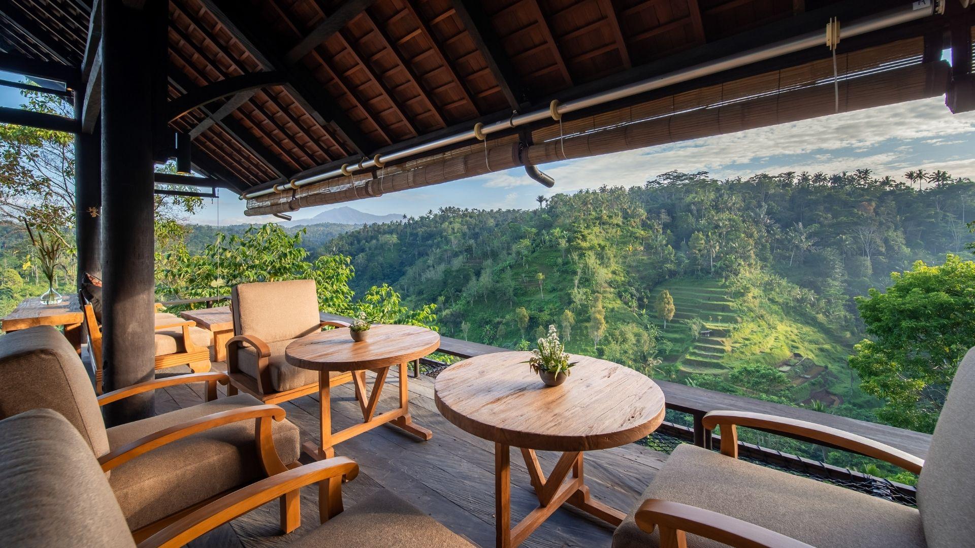 Chairs and tables  at The Botanist bar, face lush green hills under a wooden roof at Banyan Tree Escape - Buahan.