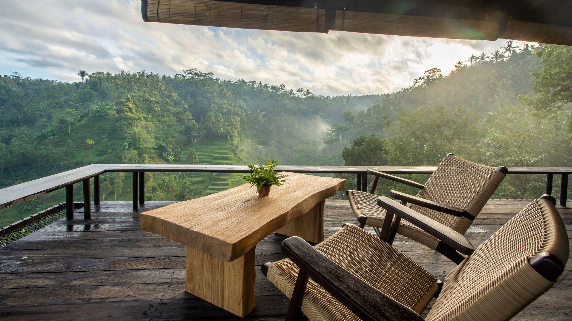 Wooden table with chairs overlook lush, green hills at Banyan Tree Escape - Buahan, The Botanist bar, .