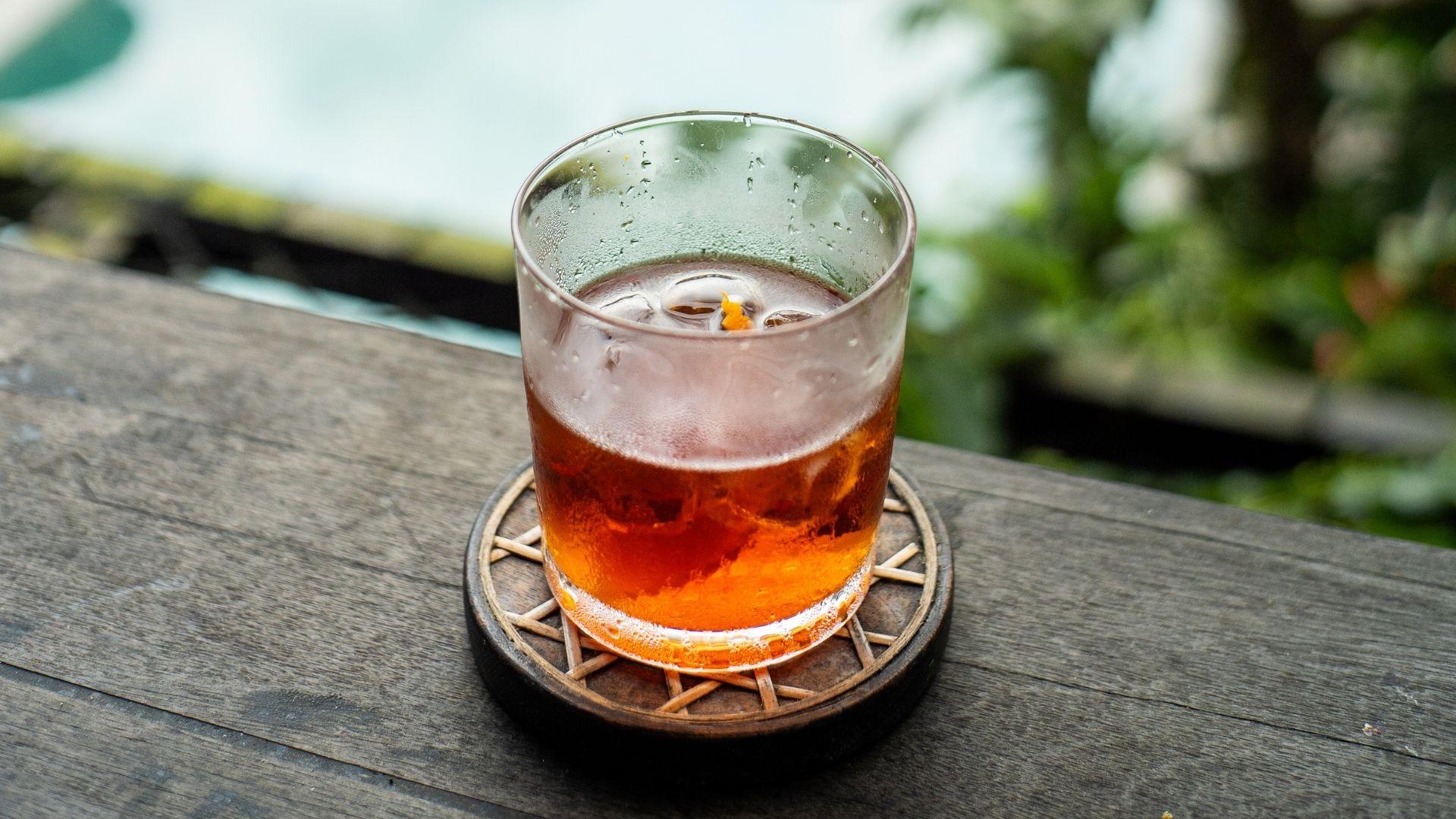 A cold drink in a glass sits on a coaster, at The Botanist bar, overlooking lush greenery at Banyan Tree Escape - Buahan.