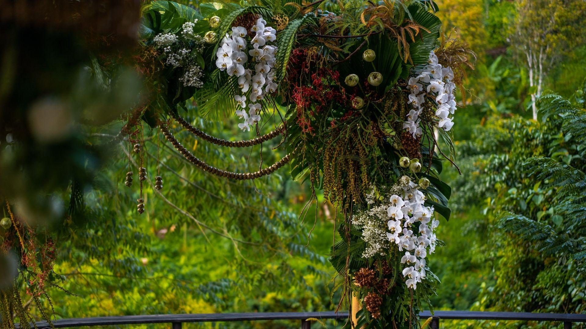 Orchid-adorned arch with lush foliage at Banyan Tree Escape - Buahan in a tropical wedding setting.