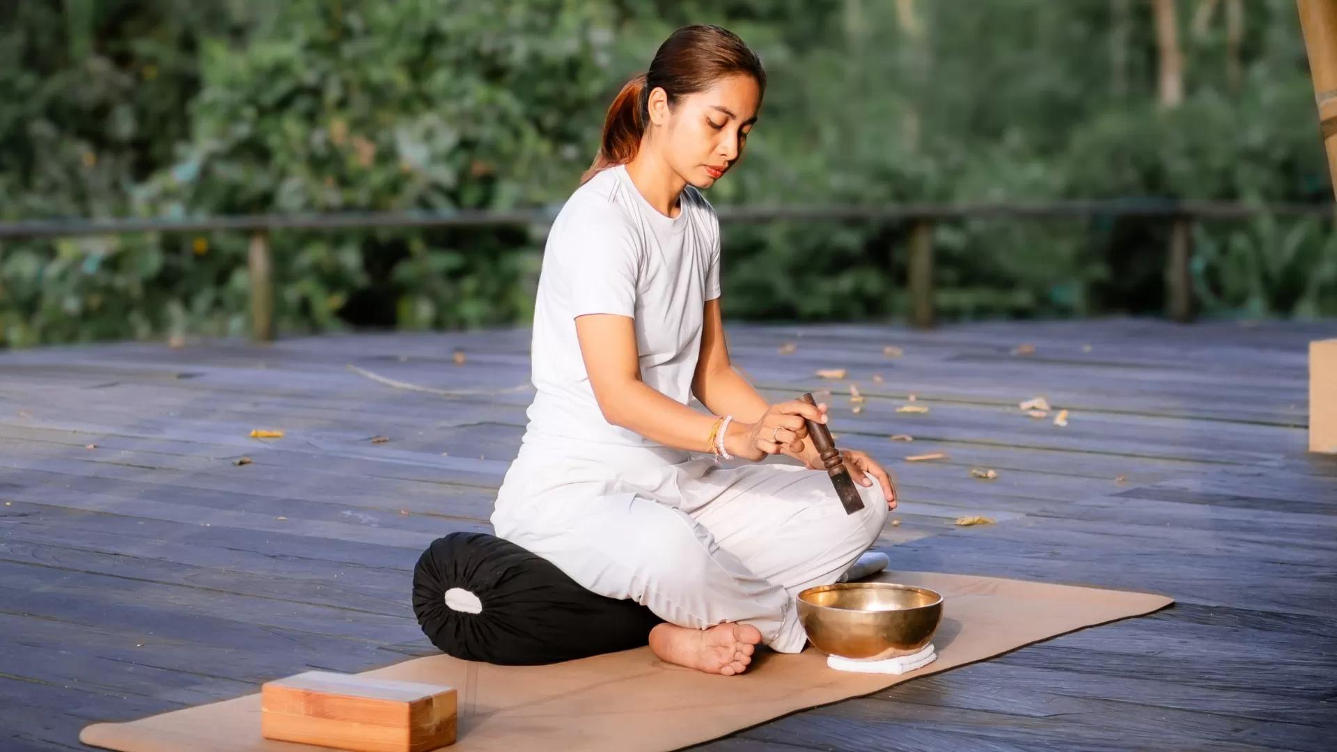 Woman meditating with sound healing and chakra on deck, surrounded by lush greenery at Banyan Tree Escape - Buahan.