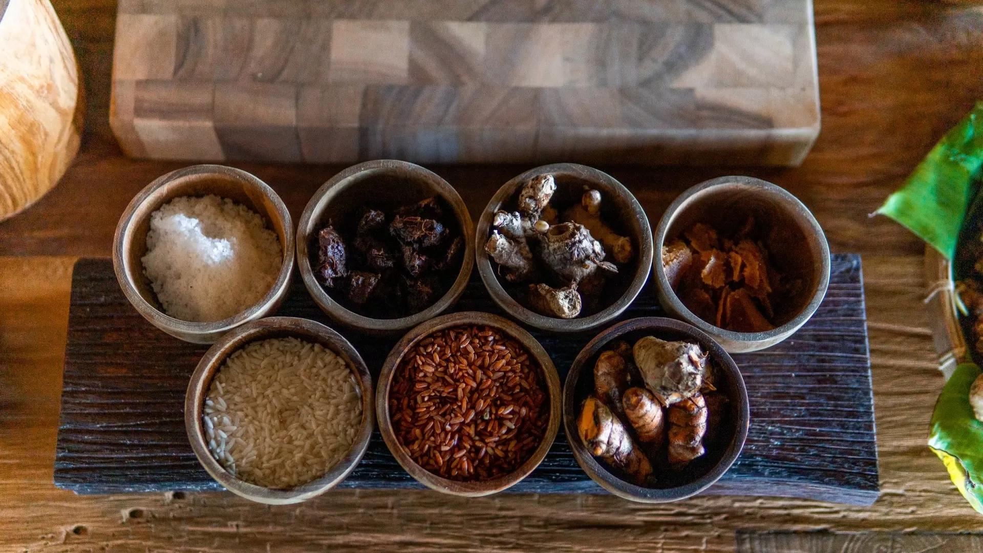 Various spices of traditional elixir Jamu, displayed in small wooden bowls on a table at Banyan Tree Escape - Buahan resort.
