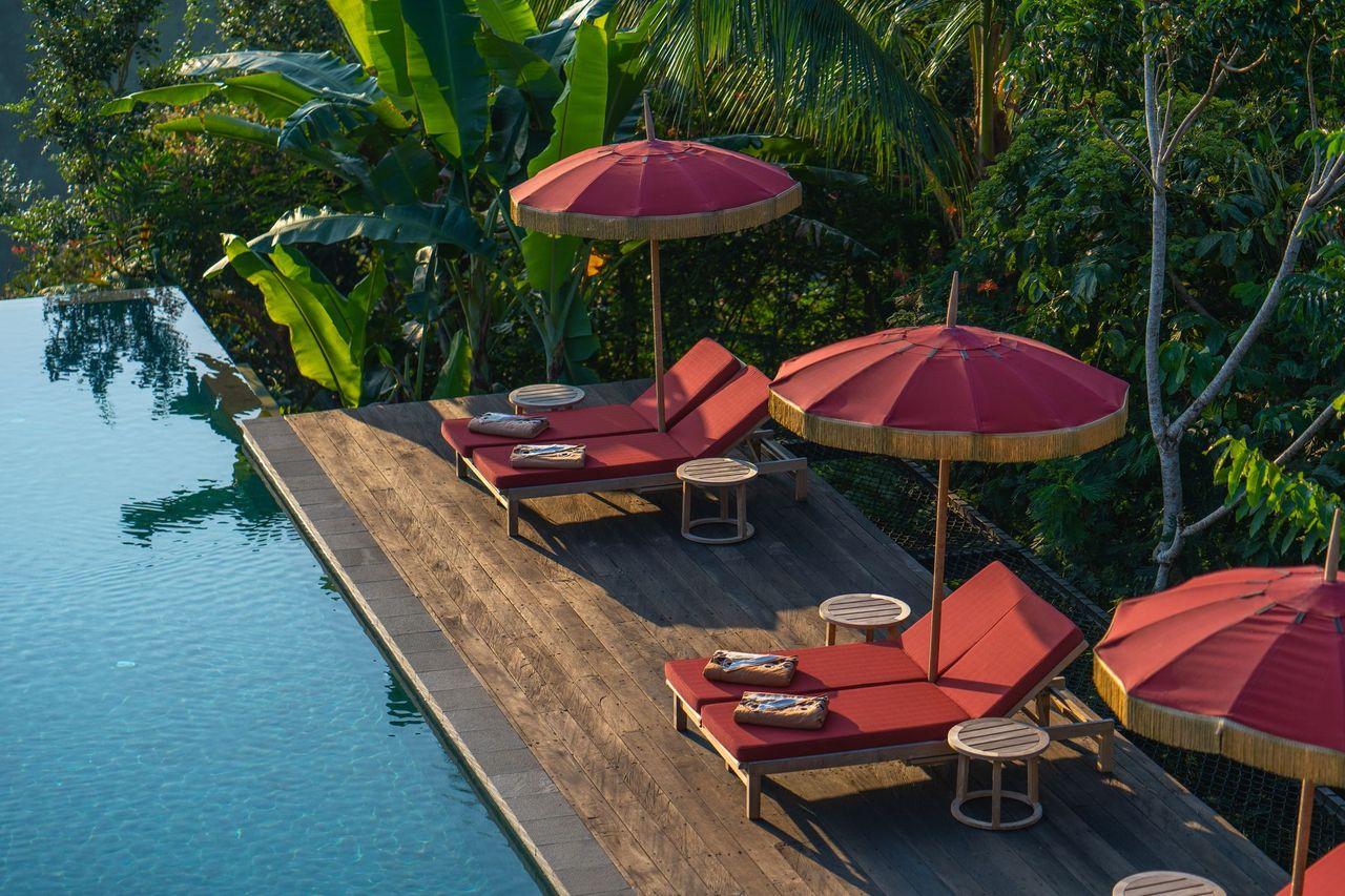 Red loungers rest under umbrellas beside a serene pool amidst lush greenery at Banyan Tree Escape - Buahan.